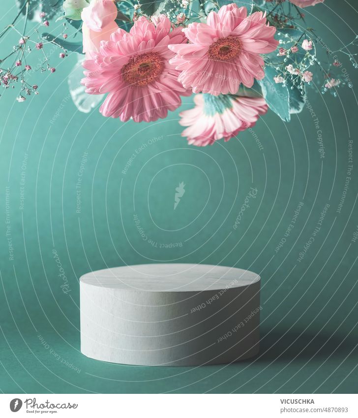 Hübsches Produktdisplay mit zylindrischem Podest und fliegenden rosa Blumen vor dunkel-türkisem Hintergrund. hübsch Produktpräsentation Zylinder Podium