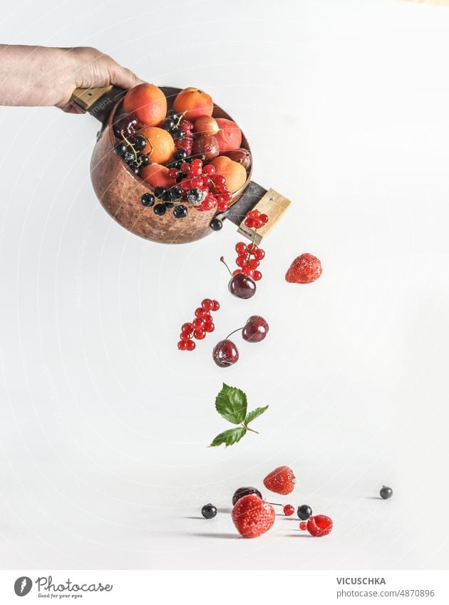 Frau Hand hält Kupfer Kochtopf mit fallenden Sommer Früchte und Beeren auf weißem Hintergrund Beteiligung kupfer Sommerfrüchte Johannisbeeren erdbeeren
