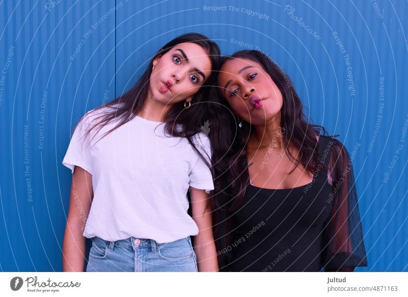 Zwei Freunde unterschiedlicher ethnischer Herkunft hören vor einer blauen Wand Musik. Mädchen Ethnizität Spanien jung Frau Zwanziger Jahre trendy