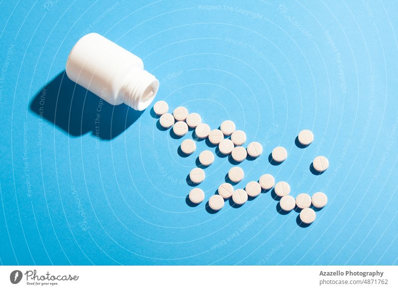 Weiße Plastikflasche und Pillen auf blauem Hintergrund mit hartem Schatten. Antibiotikum Flasche Business Kapsel Pflege Chemie Klinik abschließen Konzept