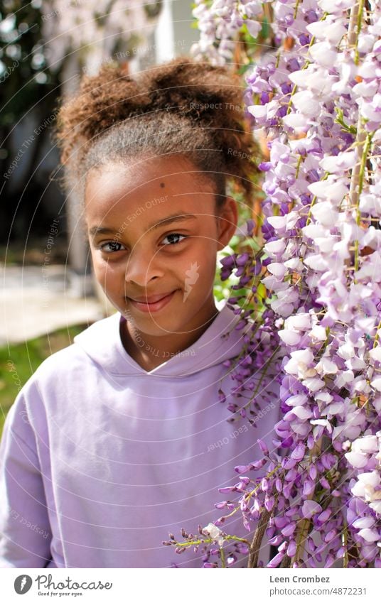 Jugendliches Mädchen gemischter Rasse mit lockigem Haar posiert zwischen lila Glyzinienblüten - Porträt Schönheit Natur Blumen Sommer Frühling Teenager