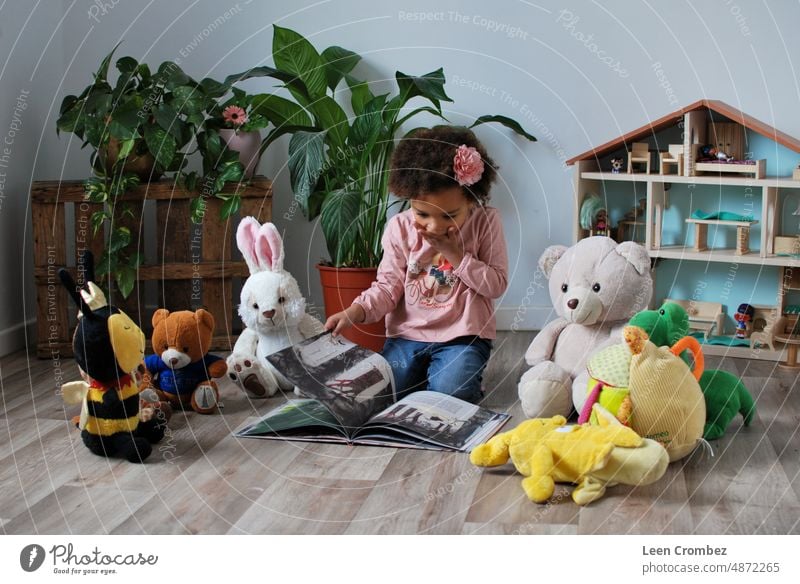 Kleines rassisch gemischtes Mädchen liest ihren Teddybären in einem Zimmer einer Wohnung eine Geschichte vor Literatur Bücher Buch Lesen eines Buches lesen