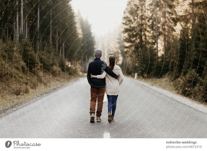 Ein verliebtes Paar spaziert auf einer schmalen Straße im Wald. Sie kuscheln beim Gehen. Gute Beziehung, aktiver Lebensstil. Gemeinsam auf dem Weg. Sie blicken in die Ferne.