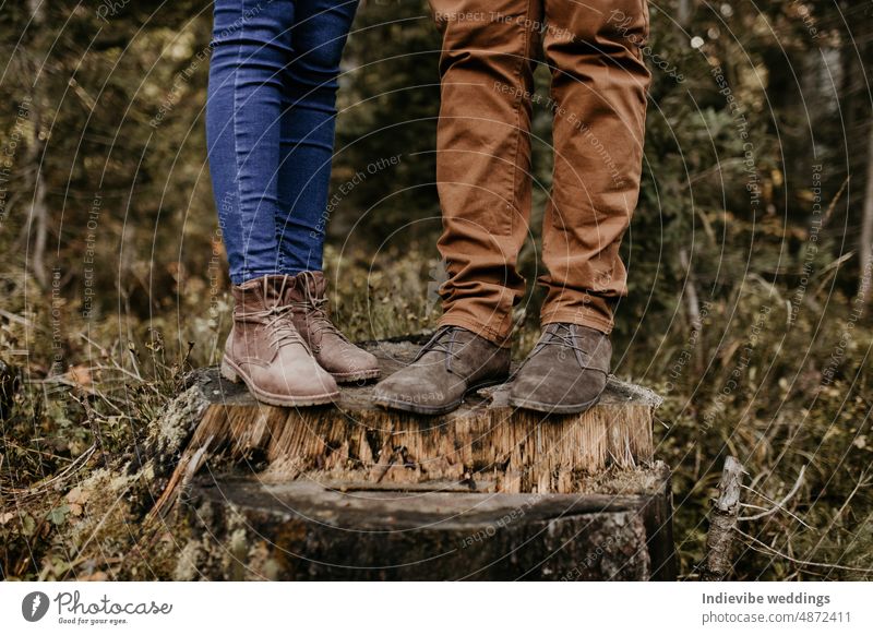 Ein Paar steht auf einem Holzstamm und ihre Stiefel und Jeans sind auf dem Foto zu sehen. Nahaufnahme ihrer Hosen und braunen Schuhe. Outdoor-Lifestyle im Wald.