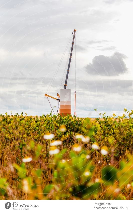 Bau und Montage einer Windkraftanlage per Kran auf einer Baustelle. Ackerland mit Bauarbeiten am Windpark in Deutschland. Energiesparkonzept aus dem Bau von Windkraftanlagen mit Wolkenhimmel