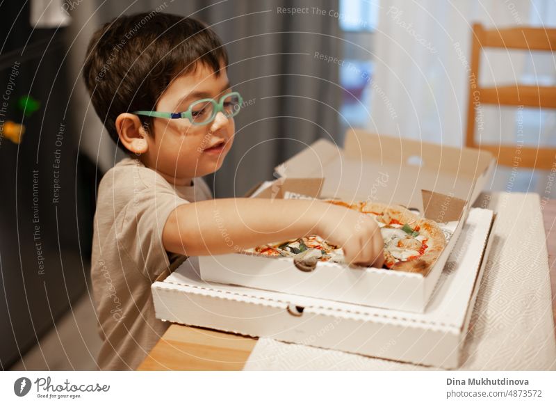 Kind von 5 Jahren alt essen Pizza aus Karton-Box zu Hause. Pizzalieferung macht Menschen glücklich. Genießen von Essen zu Hause. Junge mit Brille und Pizza.