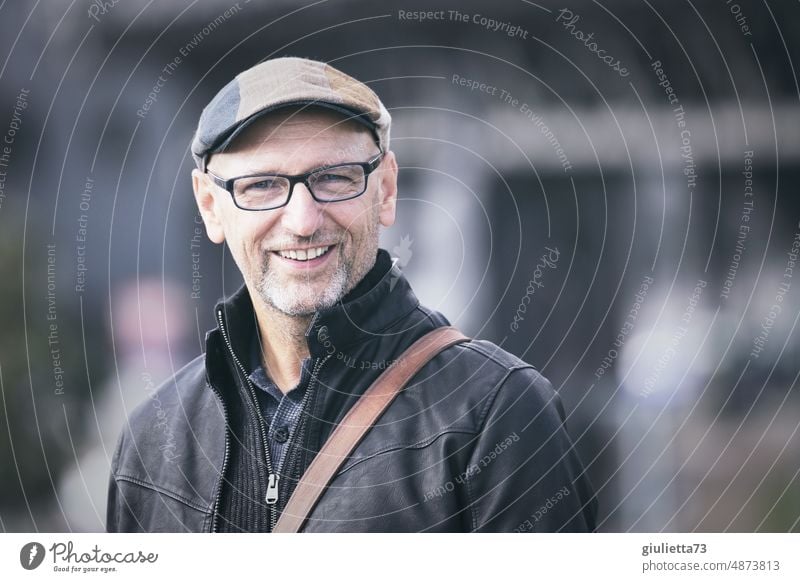 Porträt eines glücklichen, fröhlichen Mannes mit Brille, Kappe und grauem Dreitagebart | UT HH19 Zentralperspektive Schwache Tiefenschärfe Unschärfe Tag