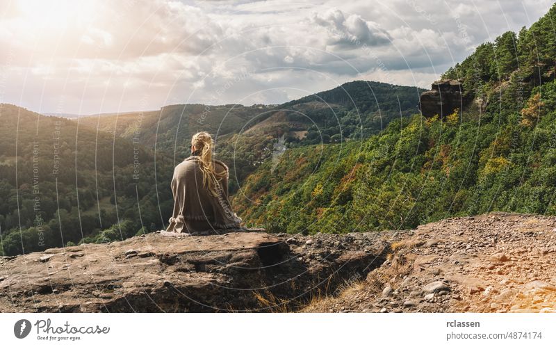 Reisende Entdeckerin, junge Frau, die auf einem felsigen Stein sitzt und auf ein Gebirgstal im Herbst blickt, Rückansicht. Berge u. Gebirge Abenteuer
