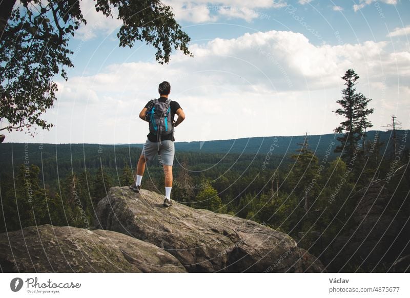 Swarthiers Männertyp steht auf einem Felsen und blickt in ein Tal in Zdarske vrchy, einem Gebirge in der Tschechischen Republik. Der Rucksacktourist genießt einen anspruchsvollen Aufstieg