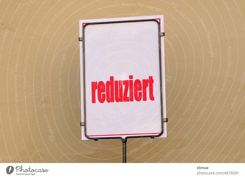 weißes Schild mit knallroter Aufschrift  - reduziert -  vor beigefarbener Hauswand / Sonderangebot / Kundenfang SSV Verkauf Handel rote Preise Sommer
