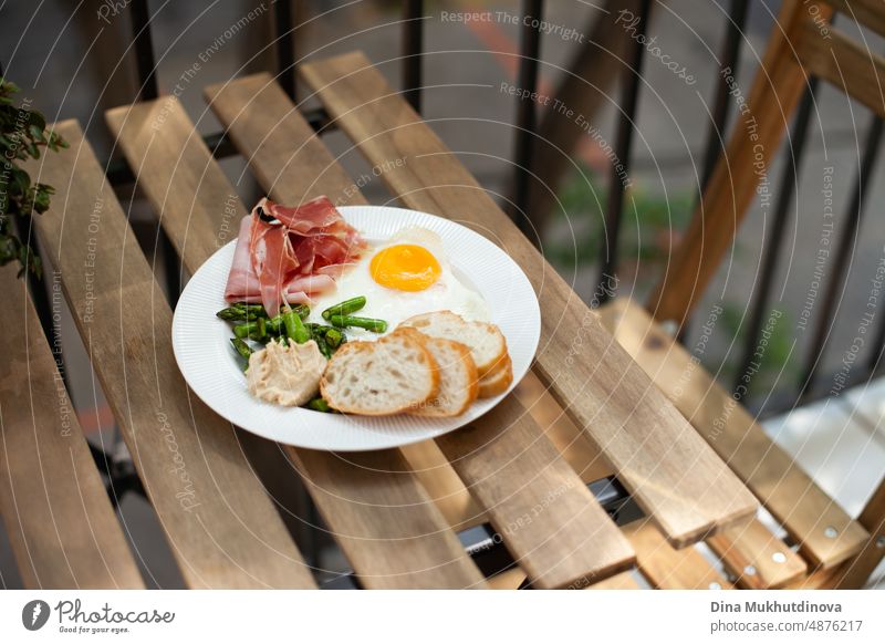 Frühstück mit Ei, Fleisch, Wurst, Spinat und Brot auf dem Holztisch auf der Terrasse. Leckeres hausgemachtes Frühstück auf dem Balkon. geschmackvoll