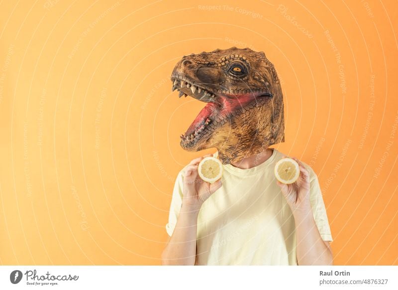 Frau mit Dinosaurierkopfmaske hält frische Zitronenscheiben auf orangefarbenem Hintergrund Person Vitamin unkenntlich Scheiben Frucht Gesundheit