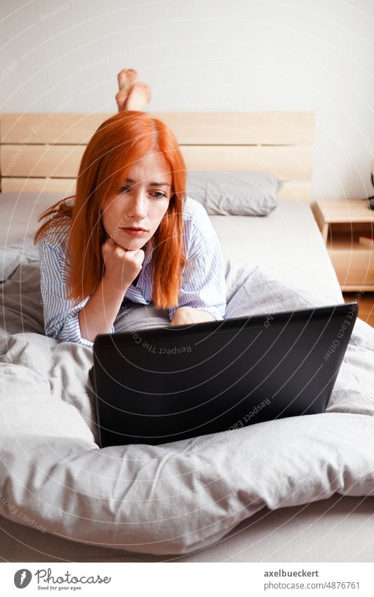 Junge Frau auf dem Bett liegend mit Laptop-Computer Lügen zuschauend Streaming Schlafzimmer heimwärts Entertainment echte Menschen Mitteilung gelangweilt