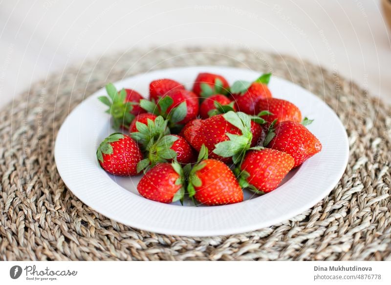 Frische rote Bio-Erdbeeren auf weißem Teller und Jute-Tischset auf dem Tisch bereit für das Frühstück. Köstliche, frisch gepflückte Beeren, nachhaltige Gartenarbeit. Wachsende Erdbeeren im Garten oder in der Wohnung.