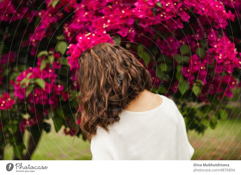 Frau brunette tanzen in der Nähe von rosa Blumen auf Baum im Sommer. Schöne glückliche Frau im Park oder Garten mit blühenden Bäumen. Frisur brünett schön