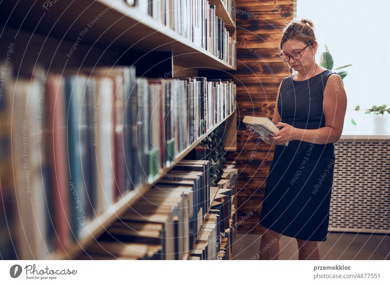 Frau liest ein Buch in einer öffentlichen Bibliothek. Auf der Suche nach Literatur zum Lesen und Lernen. Auswahl von Büchern. Vorteile des täglichen Lesens. Bücher im Regal einer Buchhandlung