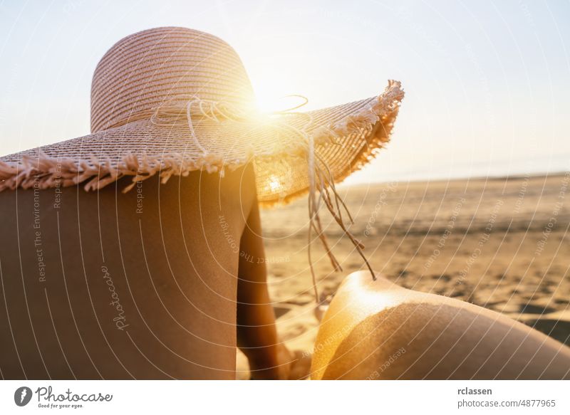 Bräunende Frau mit Sonnenhut über ihren Beinen am Strand bei Sonnenuntergang Schönheit Sand Hut Sommer lässig Top Mädchen Ansicht Haut Hintergrund Barfuß Panzer