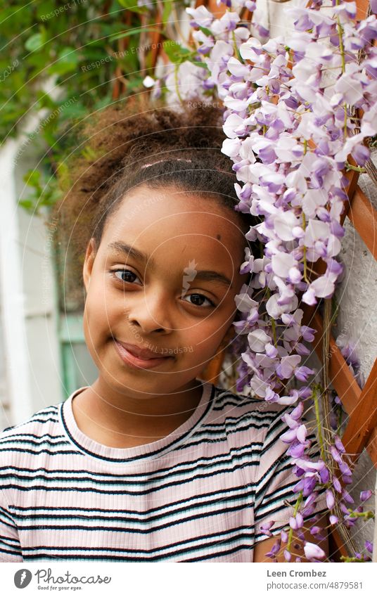 Jugendliches Mädchen gemischter Rasse mit lockigem Haar posiert zwischen lila Glyzinienblüten Teenager Schönheit gemischte Rasse Kräusel Sommer purpur Blume
