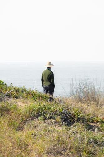 Mann mit Hut am Rande einer Klippe und Blick auf den Horizont Kontemplation Zeitgenosse Bildende Kunst weiß grau Strand Jahreszeiten Landschaft echte Menschen