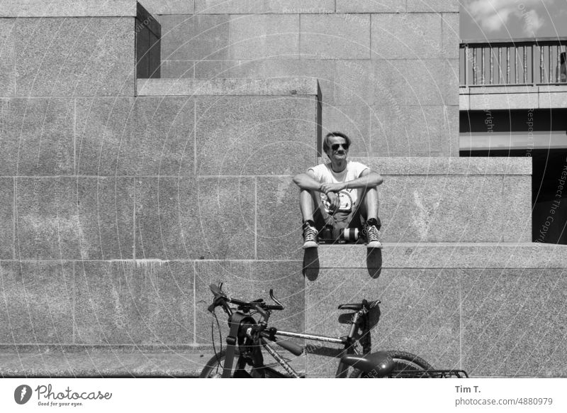 ein Mann sitzt auf einer Stufe unter ihm ein Fahrrad Rad Berlin Mitte Stadtschloss s/w bnw Tag Schwarzweißfoto Außenaufnahme Hauptstadt Stadtzentrum Architektur