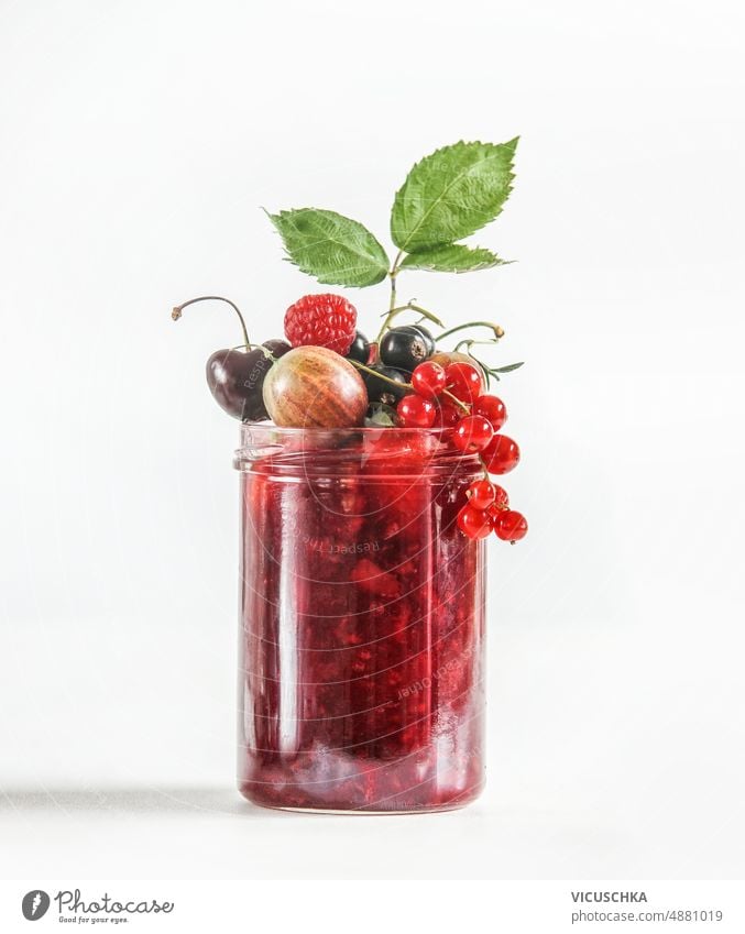 Rote Marmelade im Glas mit verschiedenen Beeren auf weißem Hintergrund. Einmachen von leckeren Sommerfrüchten. rot rote Johannisbeeren Himbeeren Kirsche
