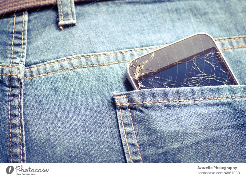 Kaputtes Handy in einer Gesäßtasche. Jeans Hintergrund mit einem gebrochenen Smartphone. Jeanshose Zelle Mobile Telefon Apparatur TFT-Bildschirm zerschlagen