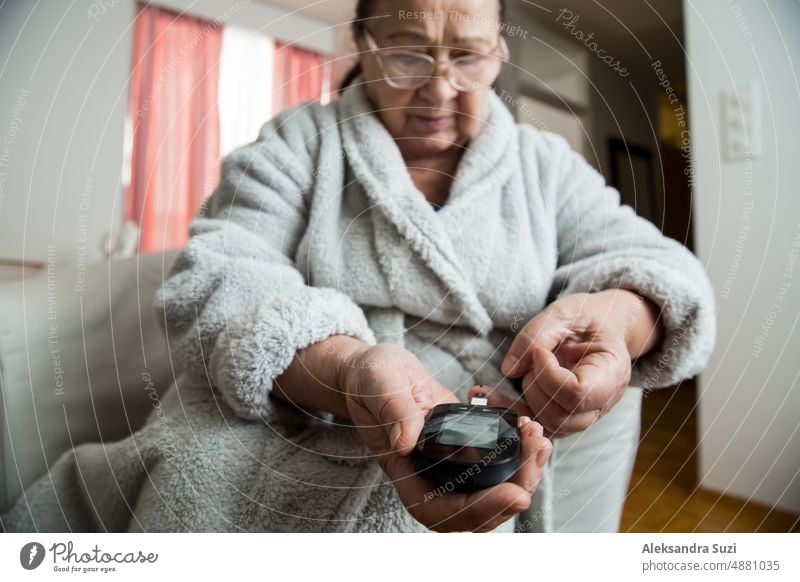 Ältere Frau, die den Blutzuckerspiegel mit einem Blutzuckermessgerät zu Hause überprüft. Alte Person mit Diabetes zu Hause im Wohnzimmer. Diabetes-Behandlung für ältere Menschen.