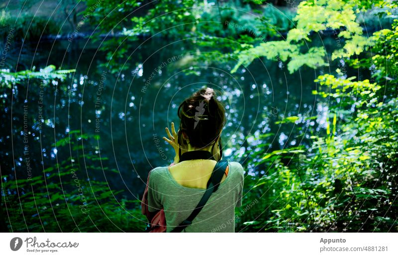 Eine junge Frau sitzt am Ufer eines Sees, ... beobachtet und fotografiert die Natur Fotografieren Fotos machen Im Grünen Licht Hobby Entspannung Wald Fotografin