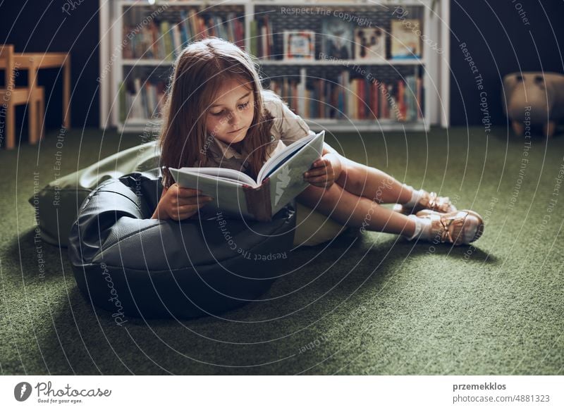 Schülerin liest ein Buch in der Schulbibliothek. Grundschülerin beschäftigt sich mit einem Buch. Kind macht Hausaufgaben. Kluges Mädchen lernt aus einem Buch. Vorteile des täglichen Lesens