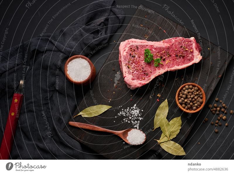 Frisches rohes Stück Rindfleisch, Striploin Steak auf schwarzem Hintergrund, Ansicht von oben. Marmoriertes Stück Fleisch Knochen Barbecue grillen Beefsteak