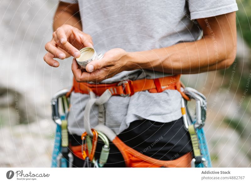Männlicher Wanderer hält Balsam stehend mit Gurt Melisse anwendend Mittelteil männlich Klettern Kabelbaum Stehen wandern Abenteuer Hand Aktivität vorbereitend