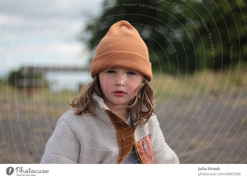 Mädchen mit oranger Mütze Kind draußen Im Freien Kuscheljacke Outdoor braune Haare Sommersprossen steiniger weg Natur Rhön Basalt Wind Porträt Außenaufnahme