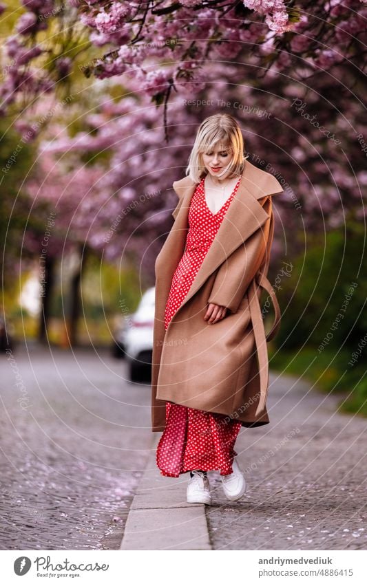 stilvolle Blondine in einem roten Kleid in der Stadt Frühling. Schönes Mädchen im roten Kleid posiert auf den Straßen der Stadt. Atemberaubende junge Frau zu Fuß in der Stadt.