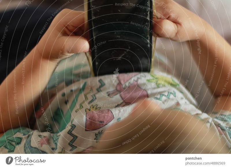 Ein Kleinkind liegt im Bett und spielt mit einem Mobiltelefon, Handy. Zerbrochene displayfolie. Kind handy mobiltelefon halten spielen mediennutzung kindheit