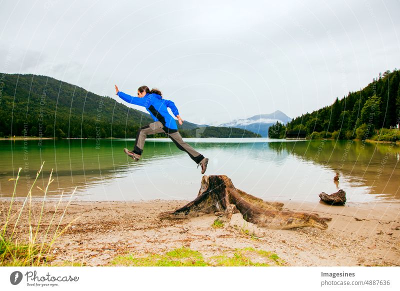 Mann springt von einem Baumstamm. Bayern Walchensee an einem regnerischen Tag. Baumstamm im Vordergrund. Europäische Alpen in Deutschland, Europa Bayerische Voralpen