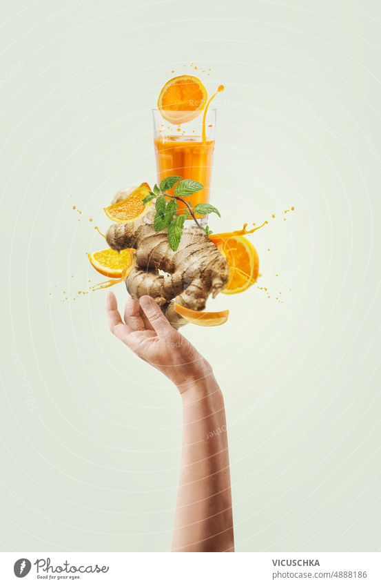 Frauenhand, die balancierenden Ingwer und orange Immunität verstärkenden Getränk mit Spritzen und Zutaten auf hellem Hintergrund hält. Hand Beteiligung