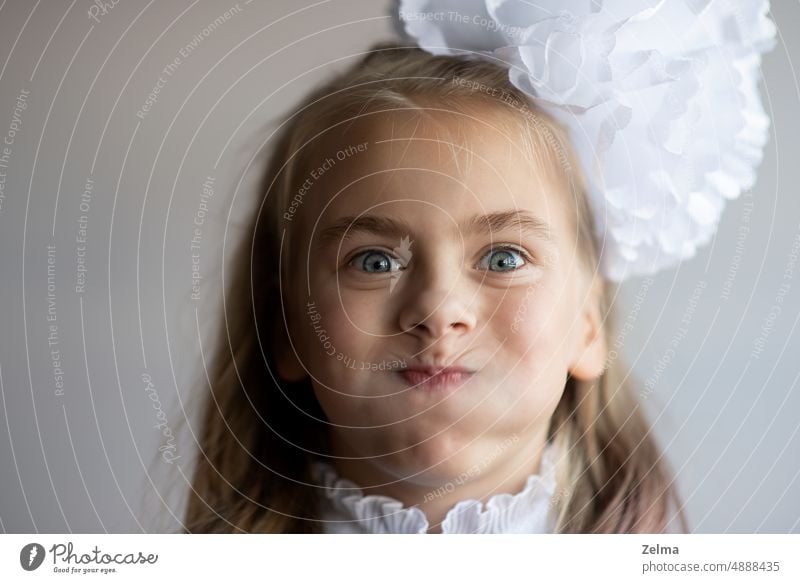 ein lustiges kleines Mädchen mit aufgeblasenen Wangen und einer weißen Schleife im Haar Gesicht Grimasse geschwollen Kind blaue Augen Porträt wirklich Menschen
