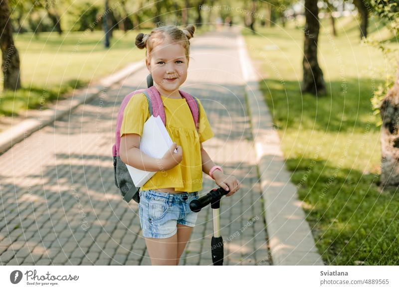Ein hübsches kleines Mädchen fährt mit dem Roller auf dem Weg zur Schule Kind wenig Tretroller Reiten Bildung Schulkind Schultasche zurück zur Schule Rucksack