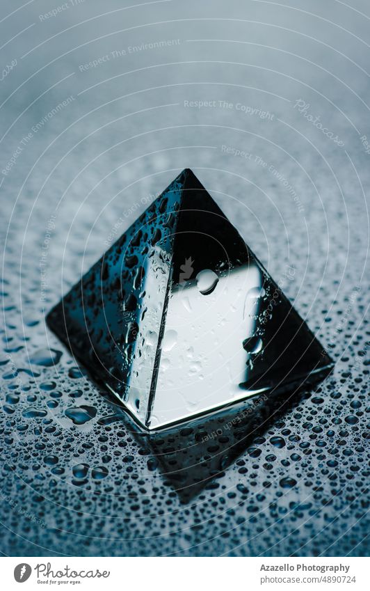 Glänzendes geometrisches Objekt mit Wassertropfen. Nasse trasparente Pyramide in Nahaufnahme. Glas Pyramiden Minimalismus Stillleben Regentropfen Tröpfchen