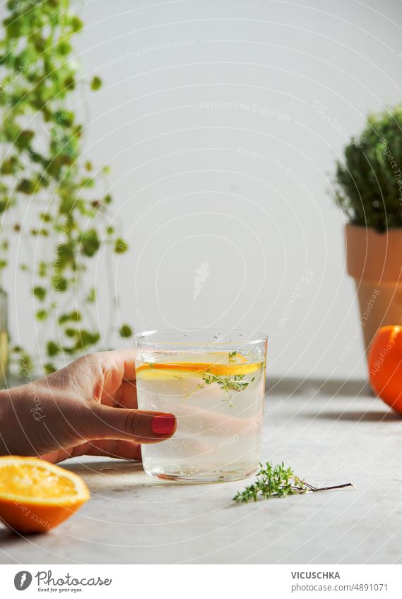 Frau hält Glas mit hausgemachter Limonade mit Orange und Thymian in der Hand Beteiligung orange selbstgemacht Küchentisch erfrischend Sommergetränk