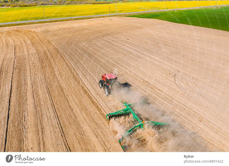 Luftaufnahme. Traktor pflügt Feld. Beginn der landwirtschaftlichen Frühjahrssaison. Cultivator Pulled By A Tractor In Countryside Rural Field Landscape. Staub steigt von unter Pflügen