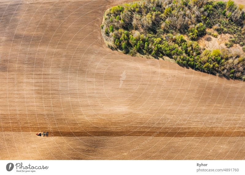 Traktor pflügt Feld im Frühling. Beginn der landwirtschaftlichen Saison. Grubber gezogen von einem Traktor in der Landschaft ländlichen Feld. Ländliches Feld Landschaft. Luftaufnahme. Top Flachansicht