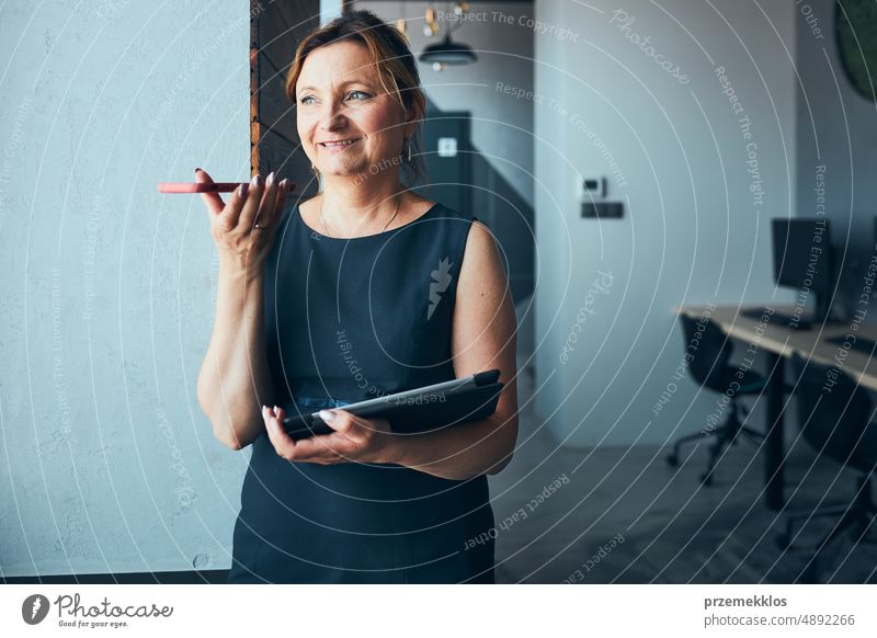Geschäftsfrau mit Geschäftsanruf arbeiten auf Tablet im Büro. Reife beschäftigte Frau mit Touchpad-Computer stehend am Fenster in modernem Interieur Smartphone