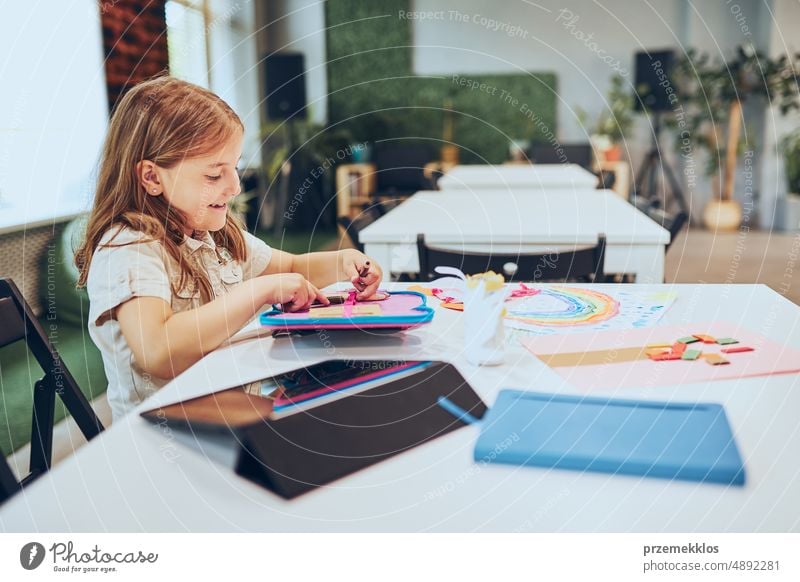 Schulmädchen macht Hausaufgaben am Schreibtisch sitzend im Afterschool Club. Mädchen malt Bilder. Lernen in der Grundschule. Grundschulunterricht. Zurück zur Schule