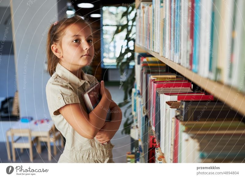 Schulmädchen schaut auf Bücherregal in Schulbibliothek. Kluges Mädchen wählt Literatur zum Lesen aus. Bücher in Regalen in einer Buchhandlung. Lernen aus Büchern. Zurück zur Schule. Schulbildung