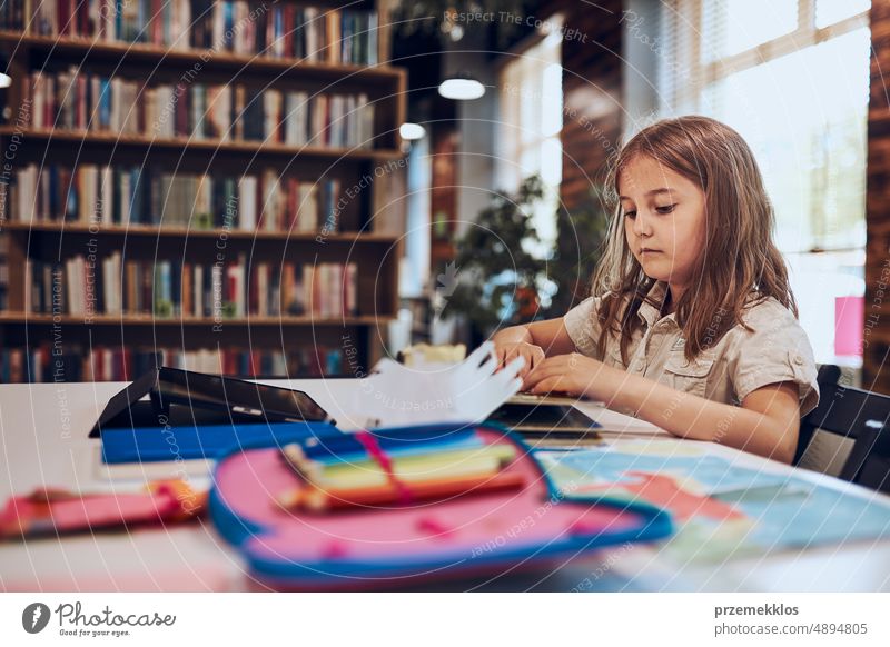 Schulmädchen beim Lernen, Spielen, Puzzeln und Lesen in der Schulbibliothek. Grundschülerin beschäftigt sich mit Buch und Puzzle. Kind neugierig Schule Rücken