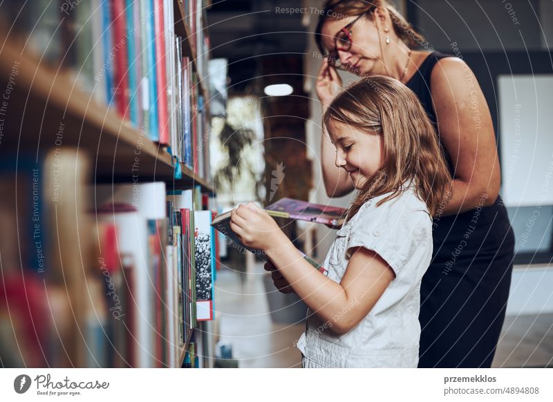 Lehrerin hilft ihrer Schülerin bei der Auswahl eines Buches in der Schulbibliothek. Kluges Mädchen wählt Literatur zum Lesen aus. Bücher in Regalen in einer Buchhandlung. Schulische Bildung. Vorteile des täglichen Lesens