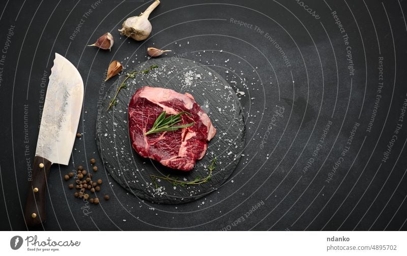 Rohe Rinderlende liegt auf einem Schneidebrett und Gewürzen zum Kochen auf einem schwarzen Tisch, Ansicht von oben Steak Lebensmittel Rindfleisch Fleisch Filet