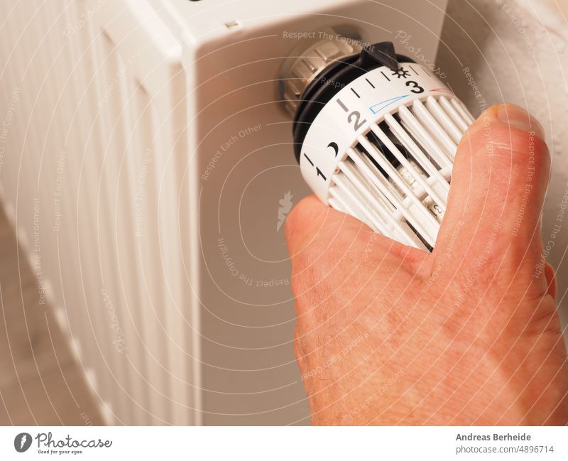 Hand dreht den Thermostat eines Heizkörpers, spart Energie, reduziert Energiekosten Komfort Energieeinsparung Heizkosten regenerativ Wandel & Veränderung Klima