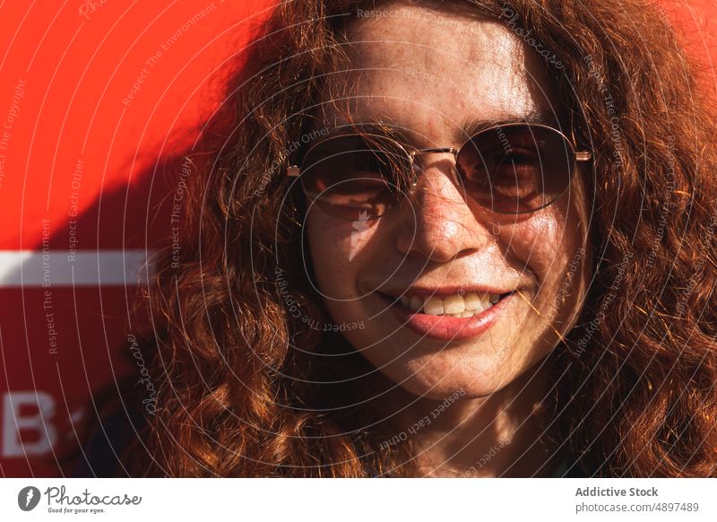 Porträt einer glücklichen Frau, die eine Sonnenbrille trägt Lächeln Wand Selbstvertrauen cool Einstellung Sonnenlicht Beteiligung Rotschopf lockig Behaarung